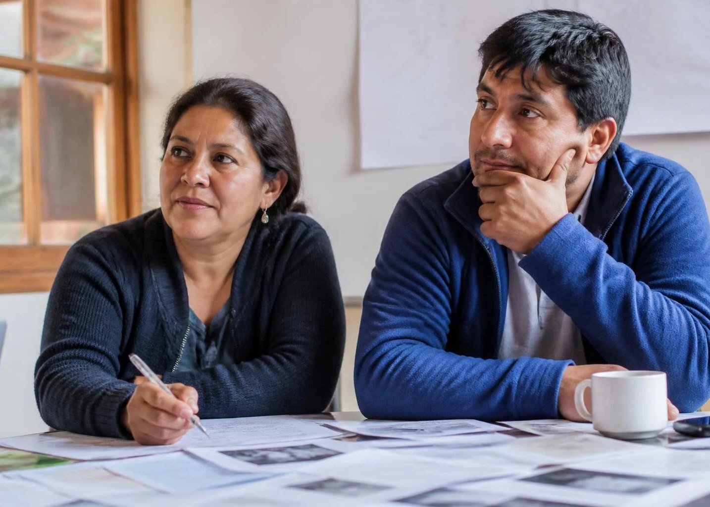 Dos adultos en una mesa de trabajo cubierta de apuntes impresos